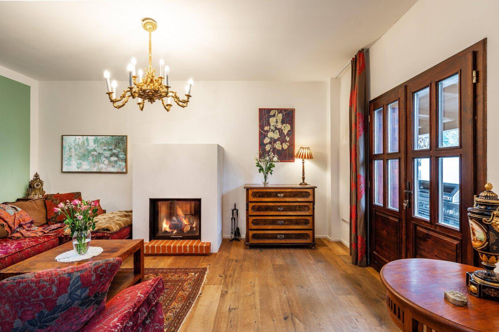 Helles Wohnzimmer mit Kamin, rotem Sofa und Holzboden, angrenzend an eine Glastür.