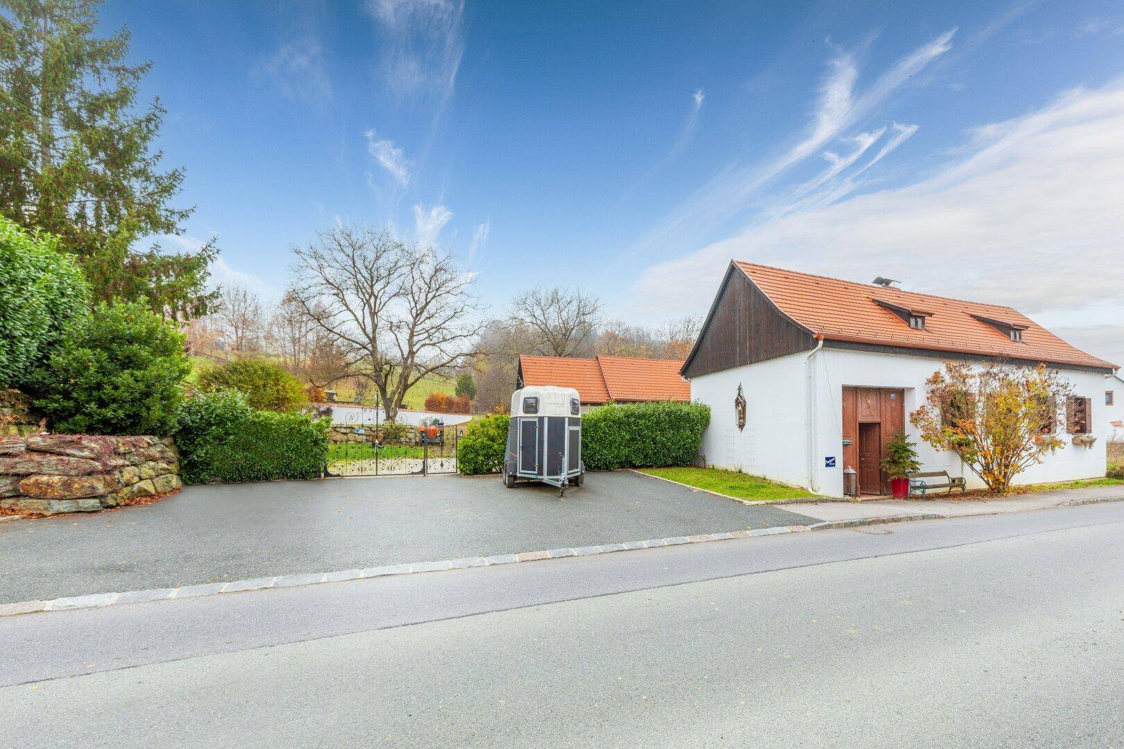 Ansicht des Anwesens von der Straße mit Parkplätzen und einem Pferdeanhänger vor dem Gebäude.