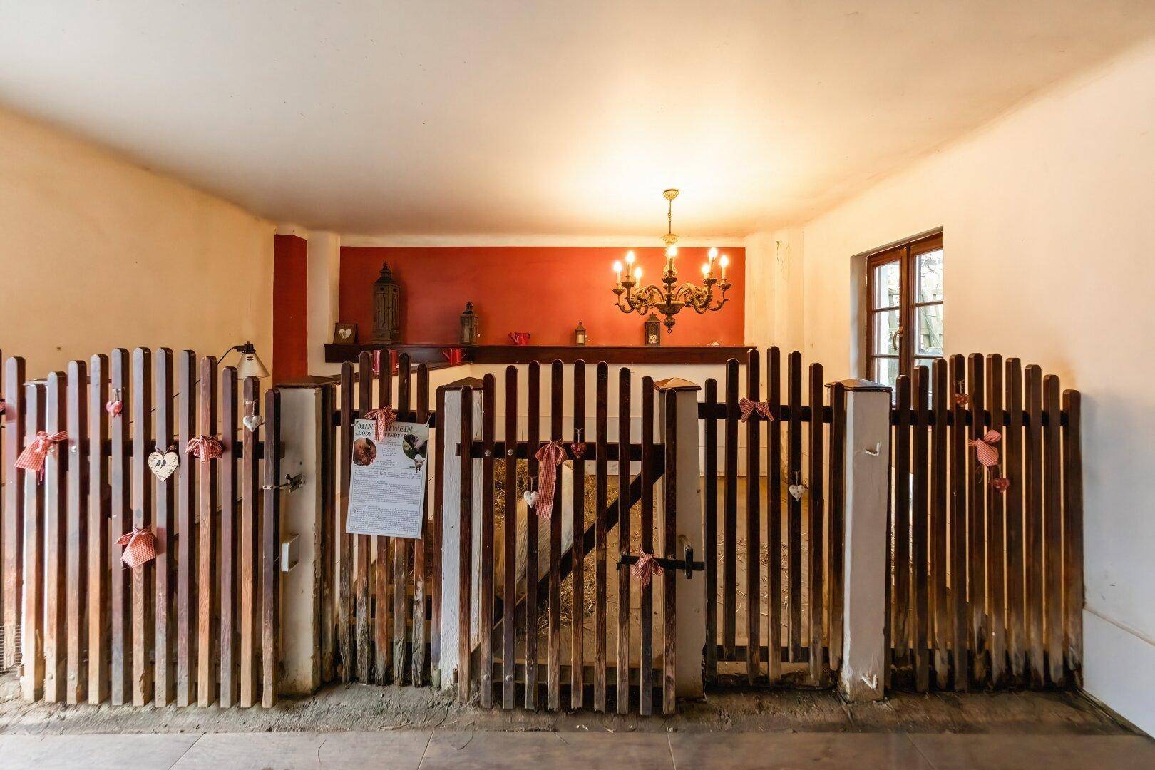 Innenraum mit Holzabtrennungen, roter Wand und Kronleuchter, möglicherweise ein Stall oder Tierbereich.