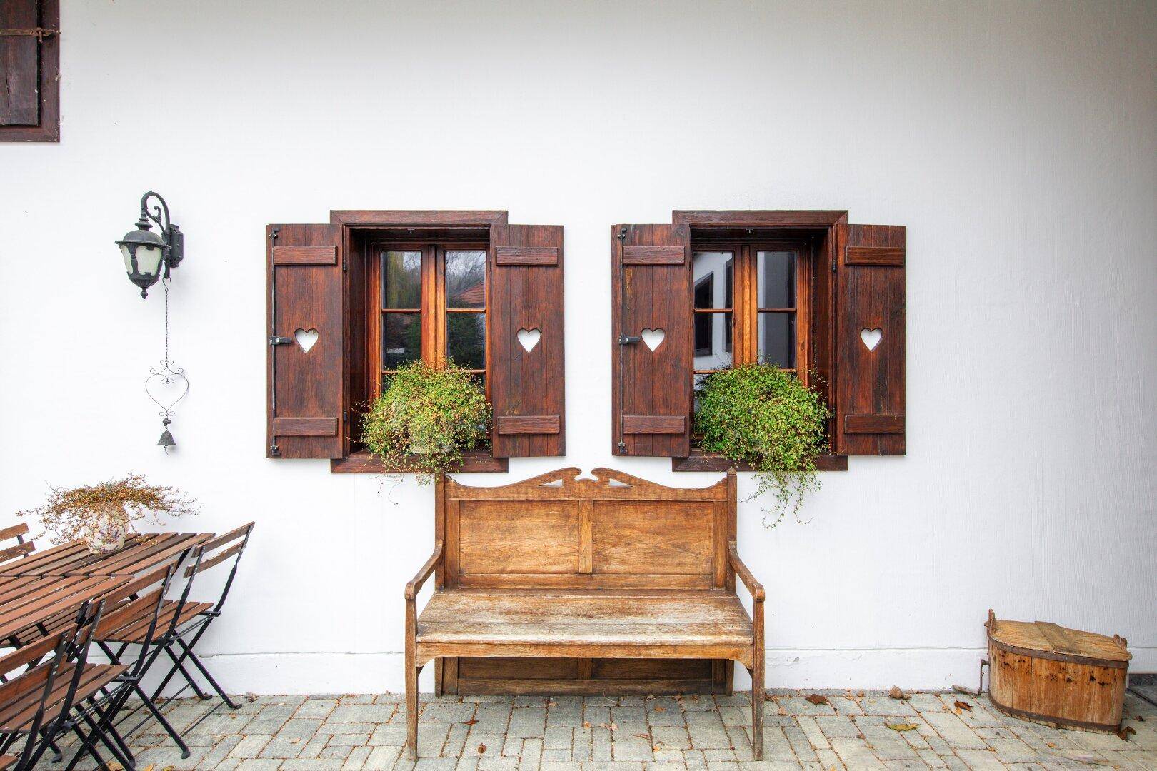 Traditionelle Holzfensterläden mit Herzmotiven und eine Holzbank im gepflasterten Innenhof.