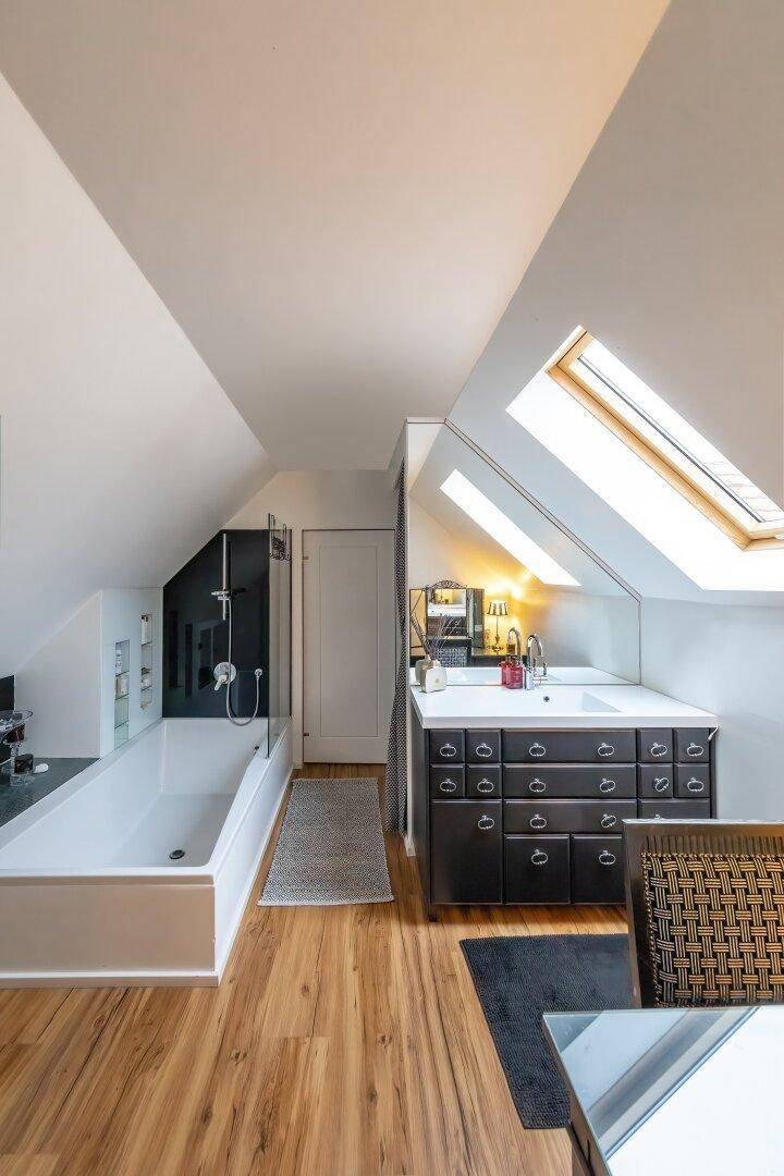 Modernes Badezimmer im Dachgeschoss mit Badewanne, Waschtisch und Dachfenstern.