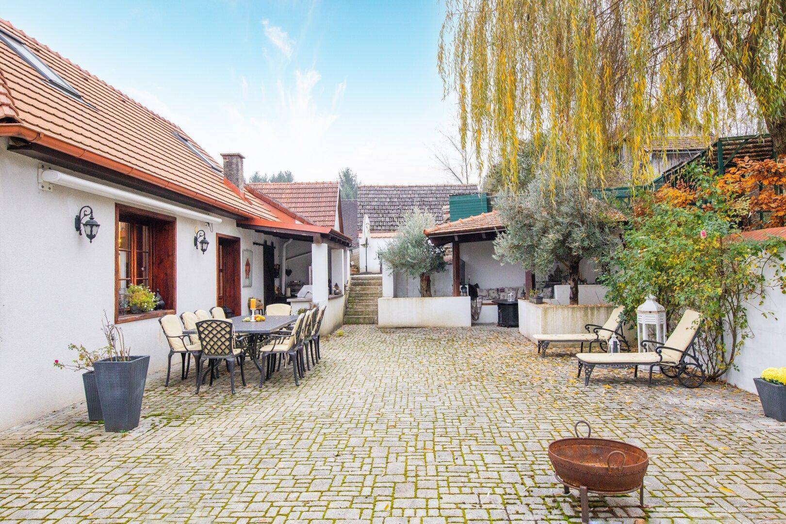 Großer gepflasterter Innenhof mit Liegestühlen, Essbereich und einem überdachten Sitzbereich im Hintergrund.