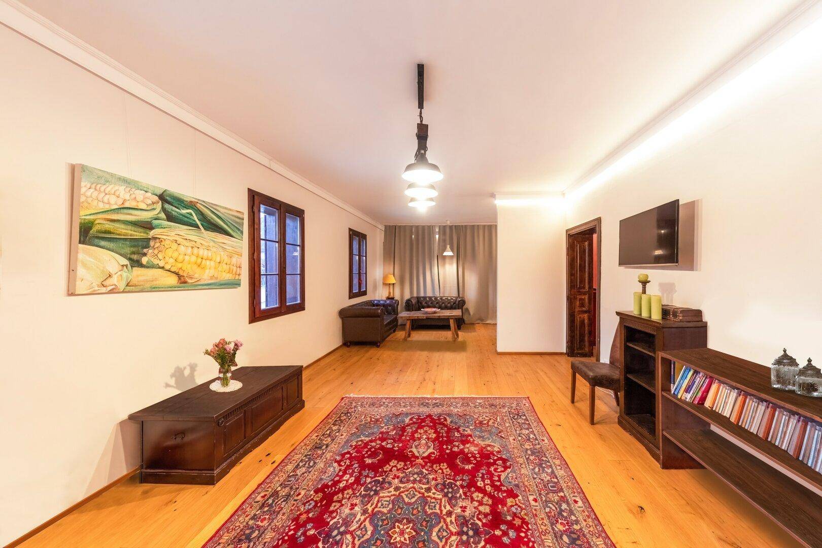 Langes Wohnzimmer mit Holzboden, Teppich und moderner Beleuchtung.