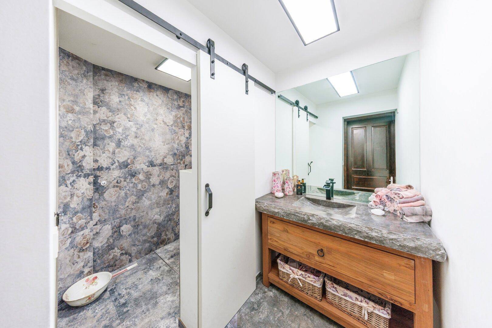 Badezimmer mit floral gemusterten Fliesen in der Dusche und Holzwaschtisch.