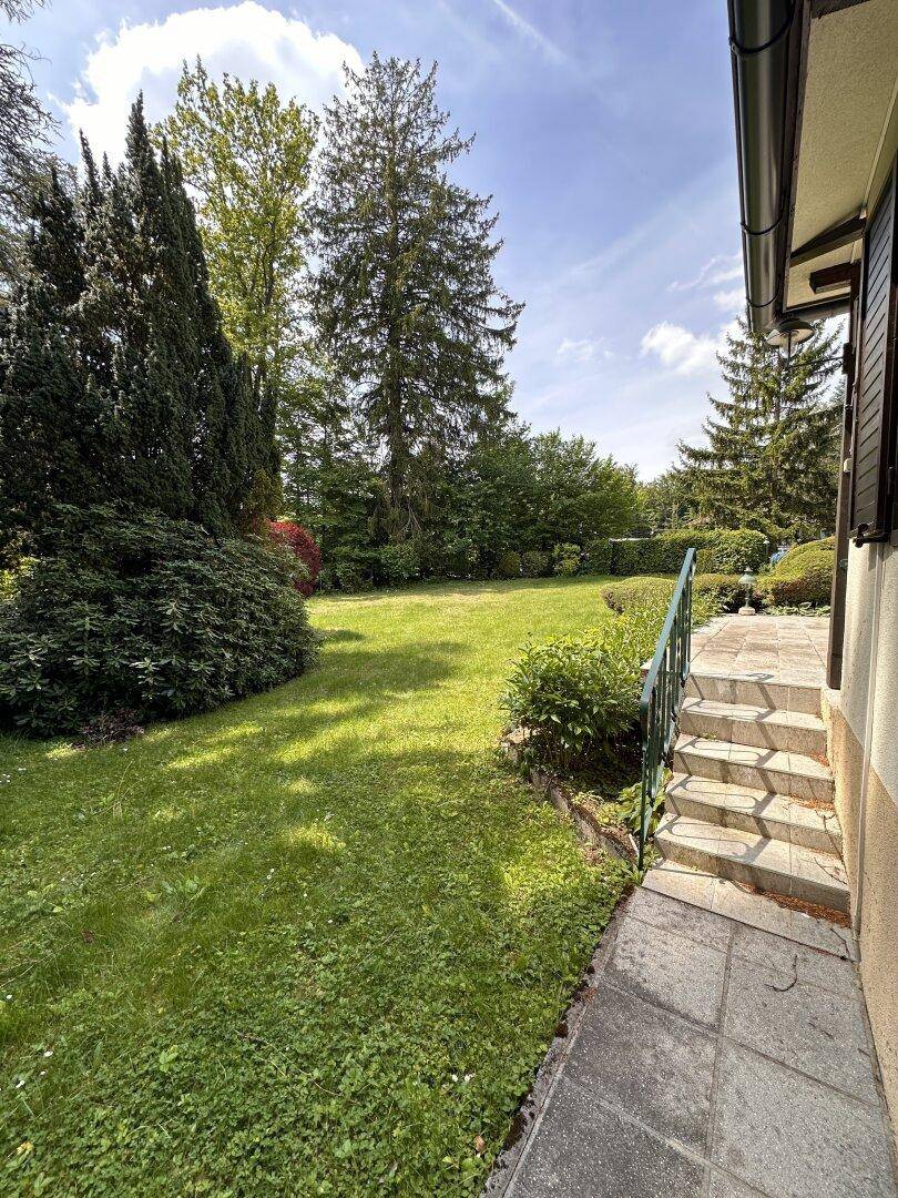 Seitenansicht des Hauses mit Zugang zum Garten, umgeben von Rasen und Sträuchern.