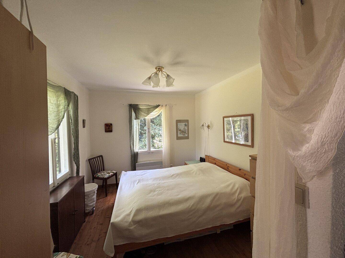 Helles Schlafzimmer mit Holzboden, einem Doppelbett und Fenstern mit Blick ins Grüne.