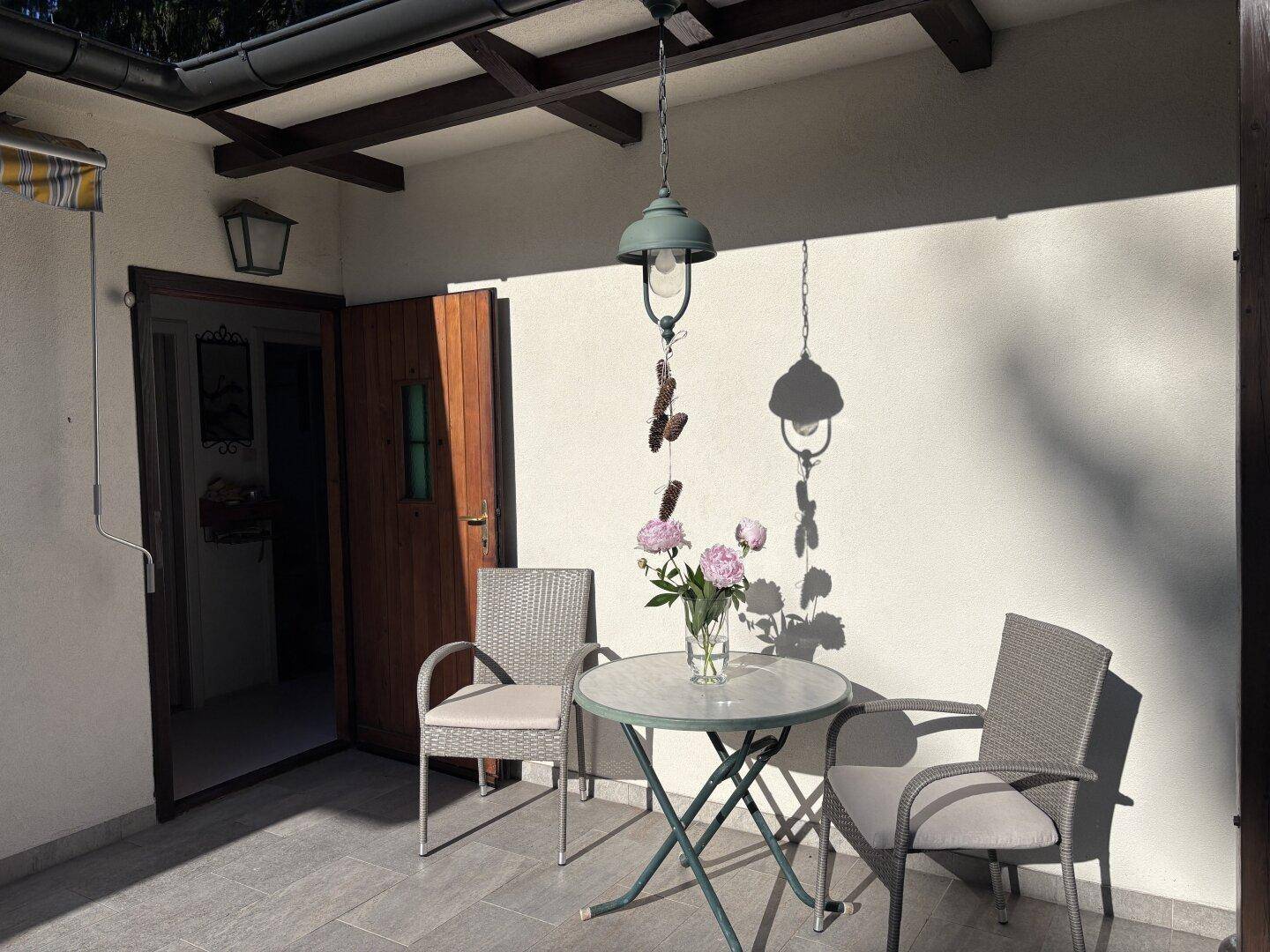 Überdachte Terrasse mit Sitzgelegenheiten und Blick auf den Garten an einem sonnigen Tag.