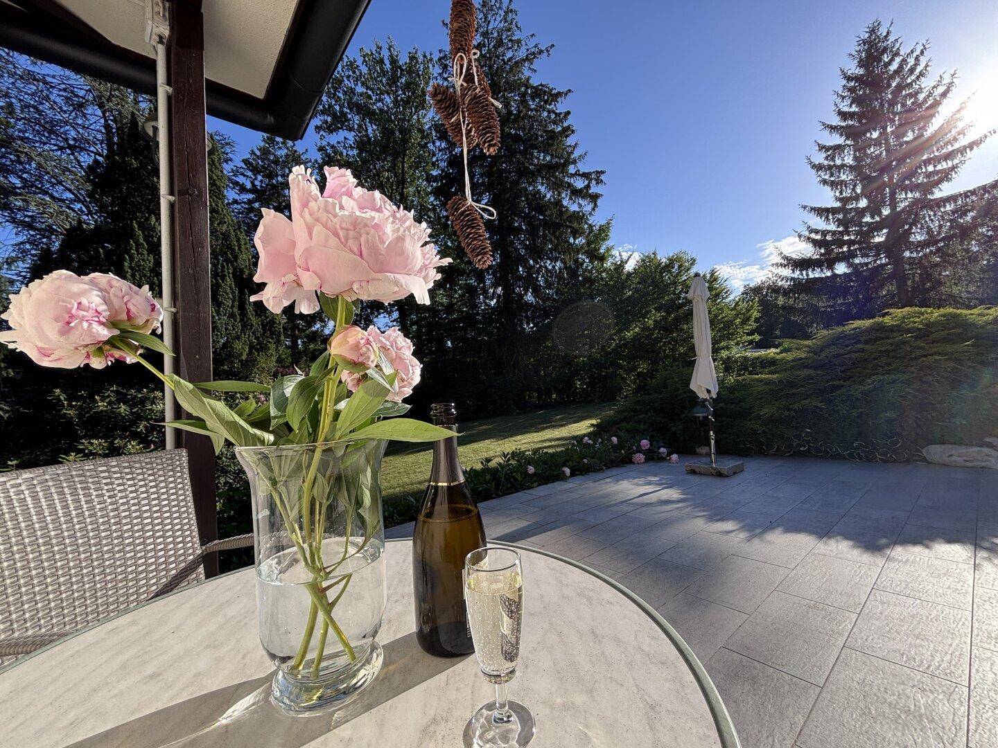 Gemütliche Terrasse mit frischen Blumen und einem Glas Sekt, umgeben von viel Grün.