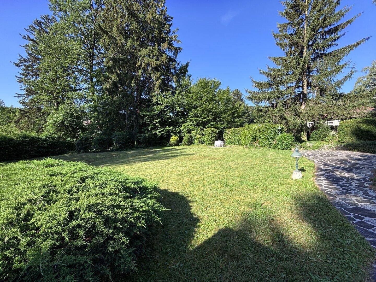 Weitläufige Rasenfläche umgeben von Bäumen und Hecken mit einem Steinweg.