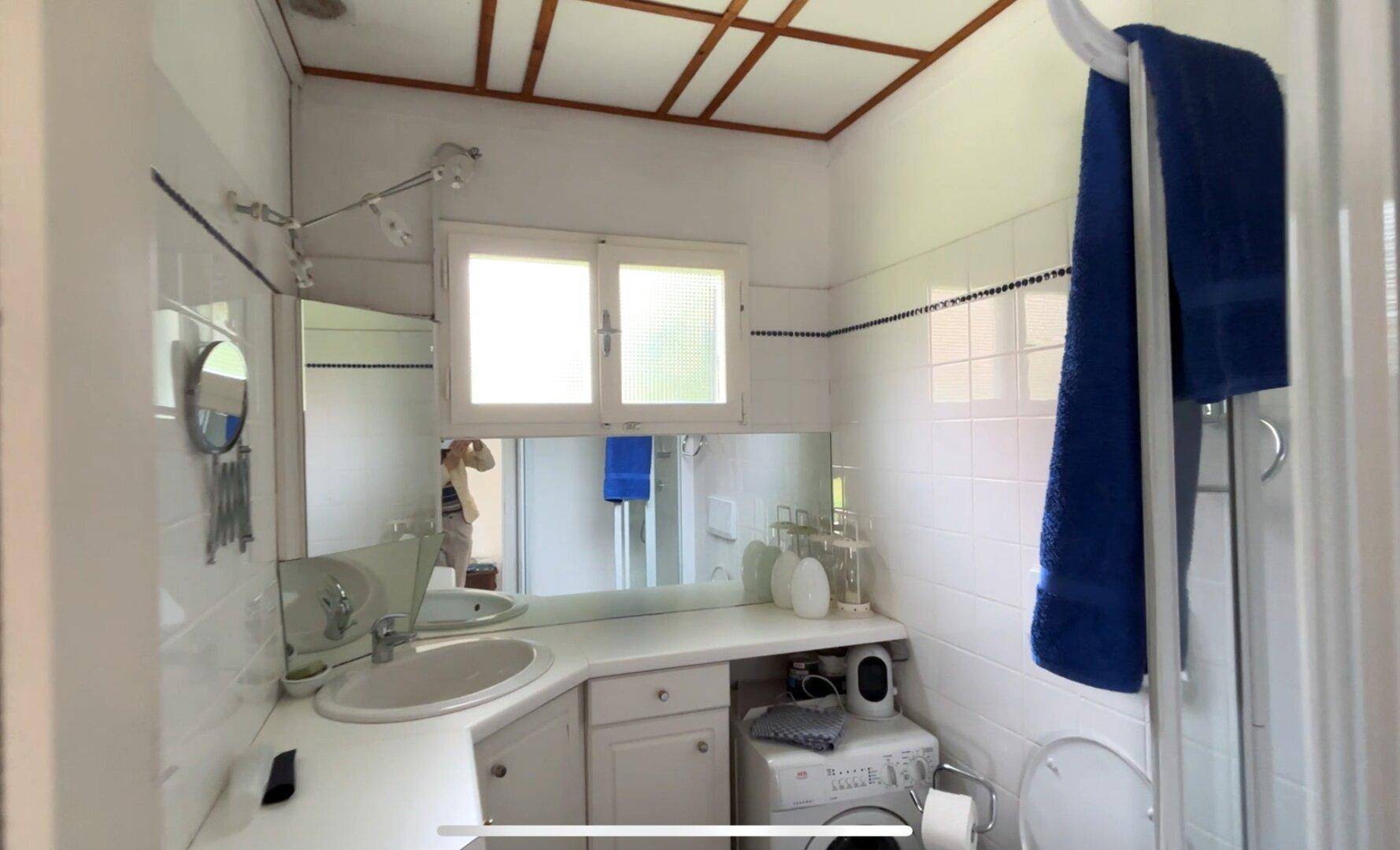 Kleines Badezimmer mit Dusche, Waschbecken und Waschmaschine unter dem Fenster.