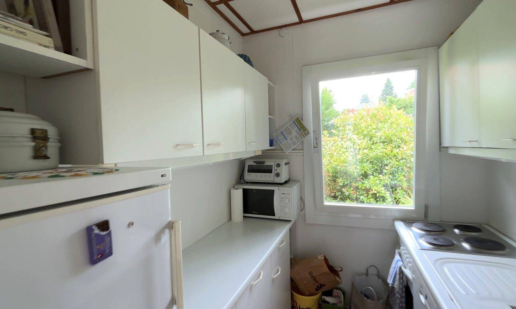 Kleine Küche mit weißen Schränken, Elektroherd und Fenster mit Blick in den Garten.