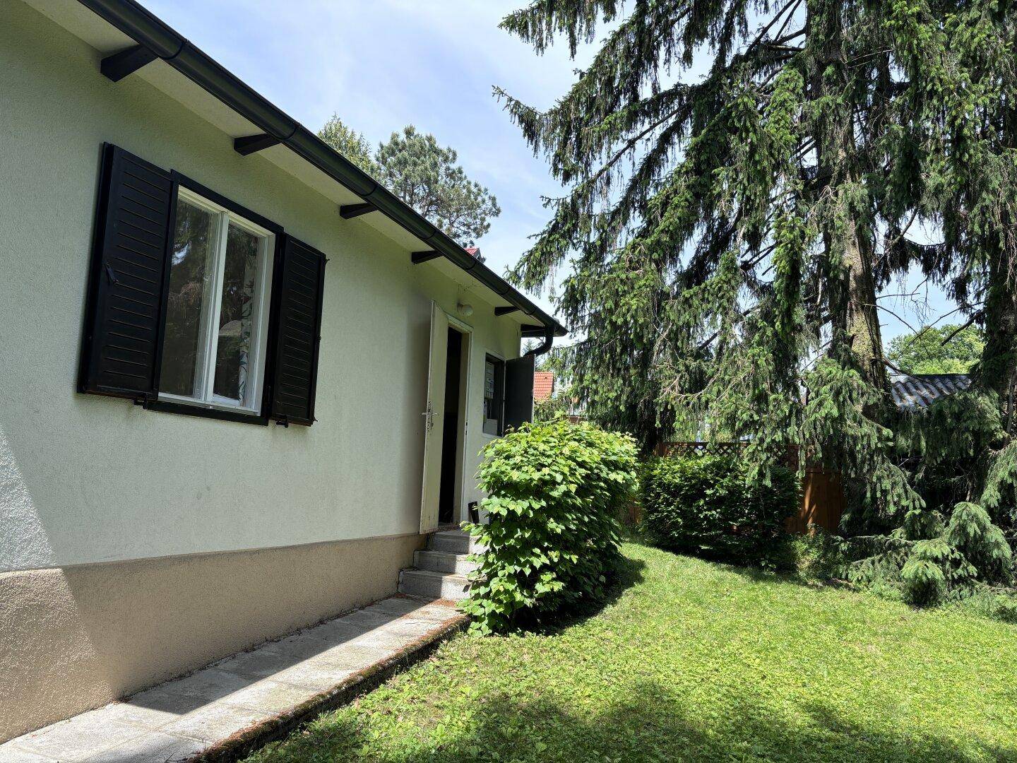 Seitenansicht des Hauses mit Fensterläden und Zugang zum gepflegten Gartenbereich.