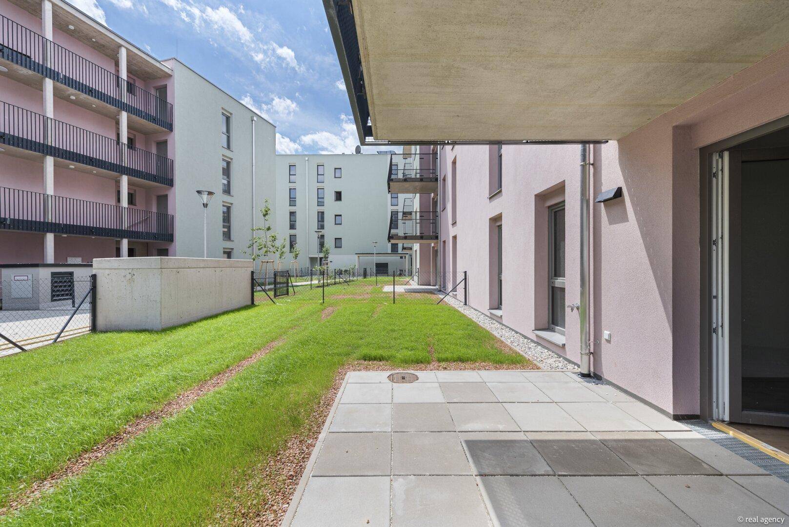 Private Terrasse mit Zugang zum Gemeinschaftsgarten und Blick auf die umliegenden Neubauten.