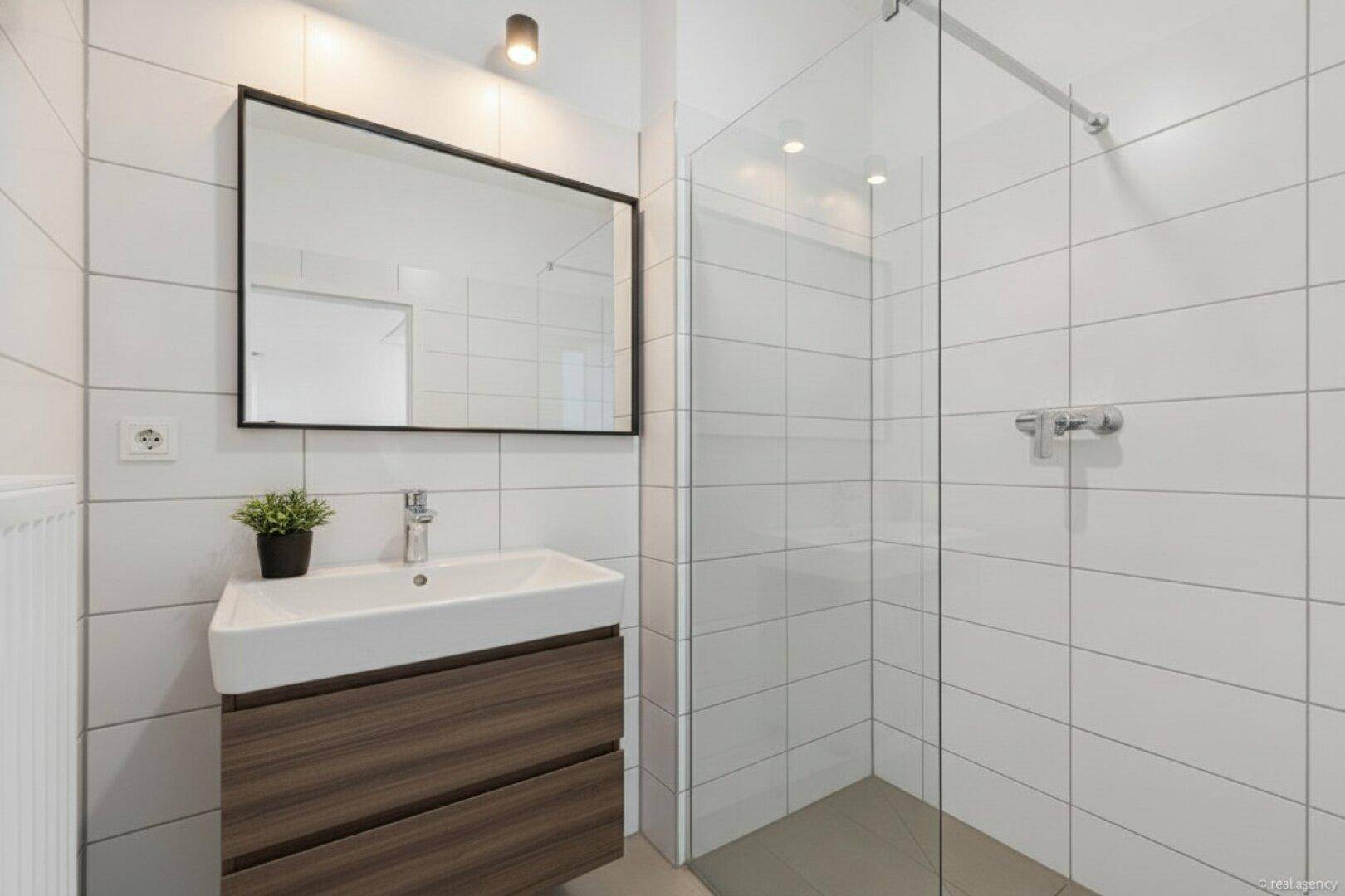 Modernes Badezimmer mit weißen Fliesen, Einzelwaschbecken und einer geräumigen Duschkabine.