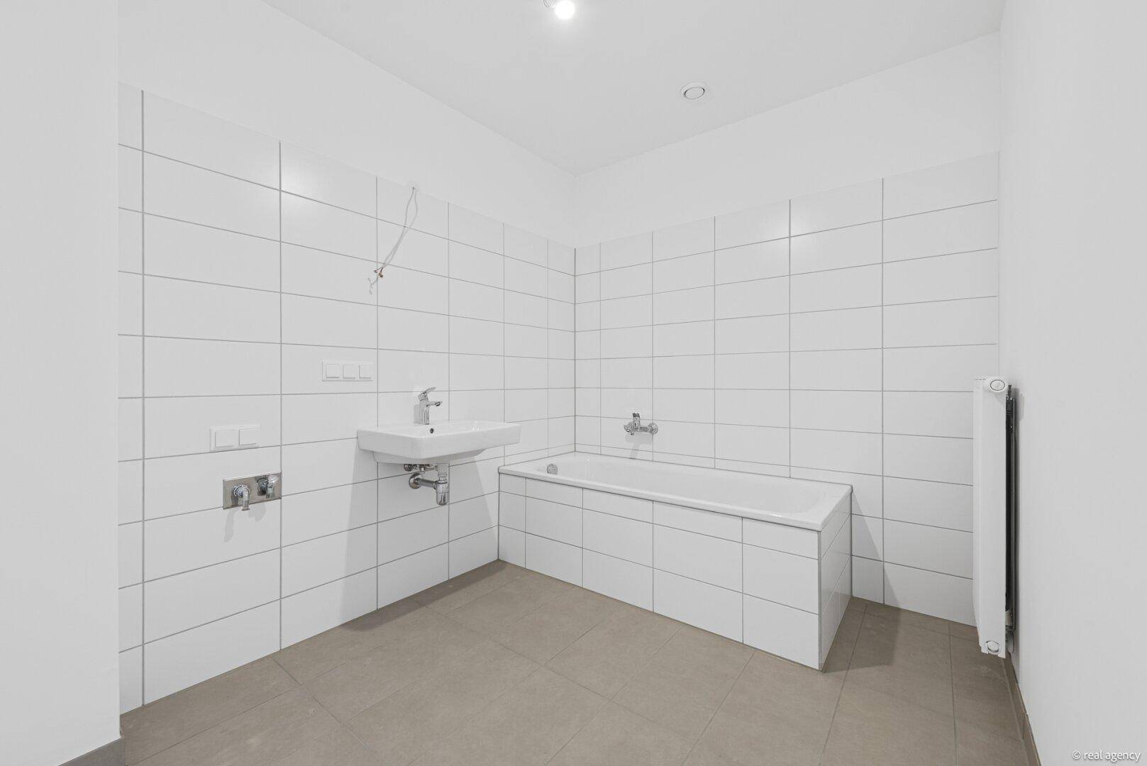 Helles Badezimmer mit weißen Fliesen, Waschtisch und Badewanne, bereit zur individuellen Gestaltung.