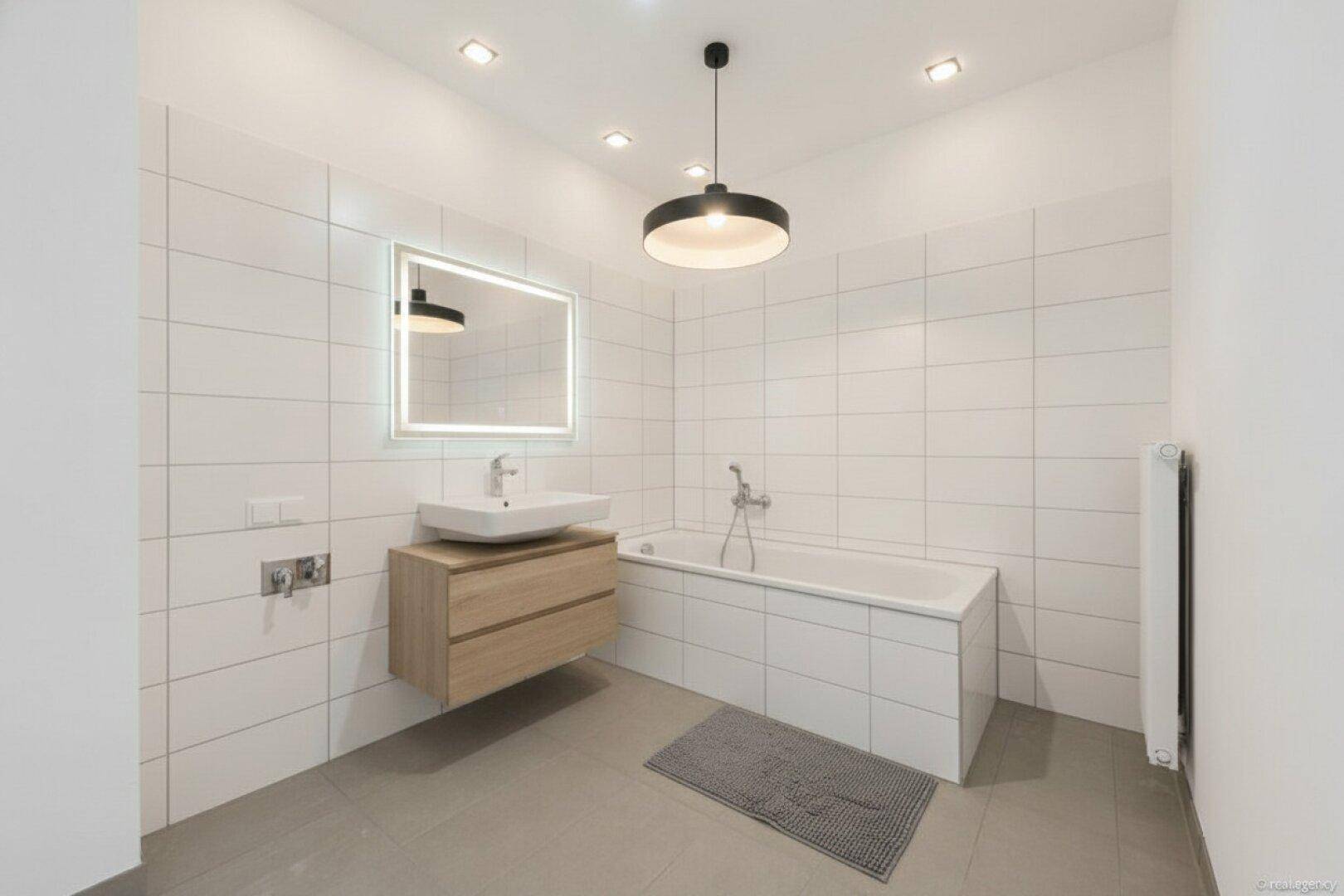 Modernes Badezimmer mit schwebendem Waschtisch, beleuchtetem Spiegel und Badewanne.