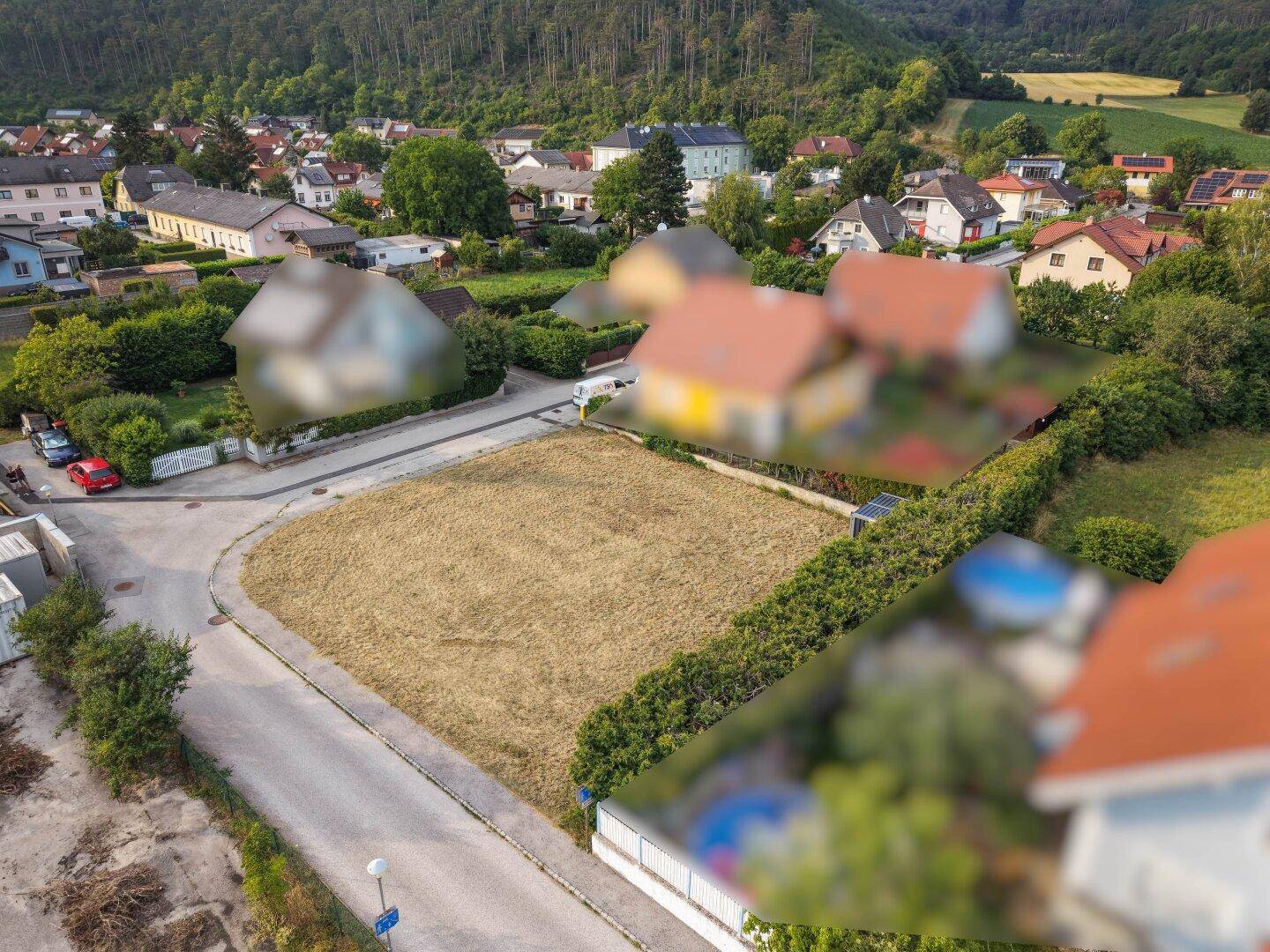 Weitläufige Luftaufnahme eines Baugrundstücks in ländlicher Umgebung mit bewaldeten Hügeln im Hintergrund.