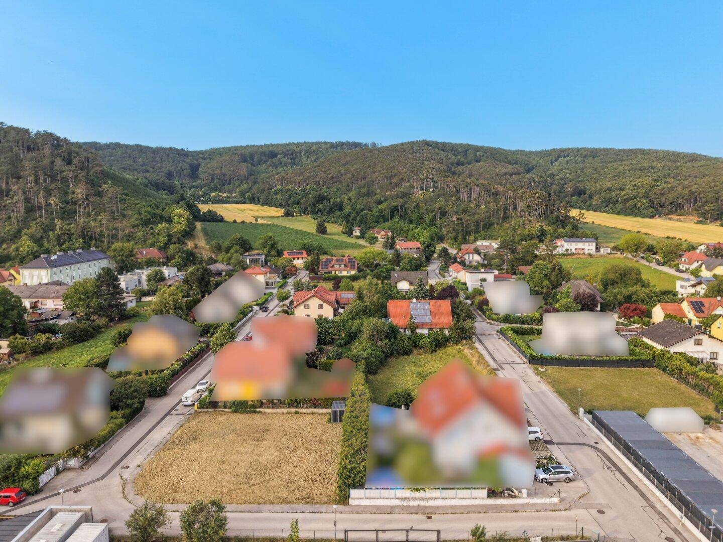 Panoramische Luftaufnahme eines Baugrundstücks mit Blick auf ein Dorf und weite bewaldete Hügellandschaften.