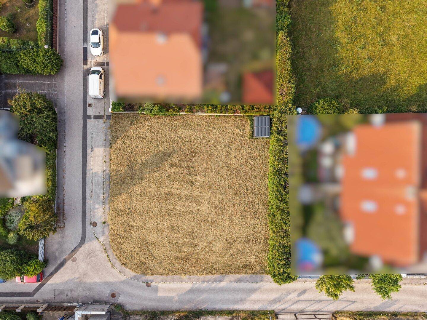Direkte Draufsicht auf das unbebaute Grundstück, umgeben von Hecken und angrenzenden Straßen.