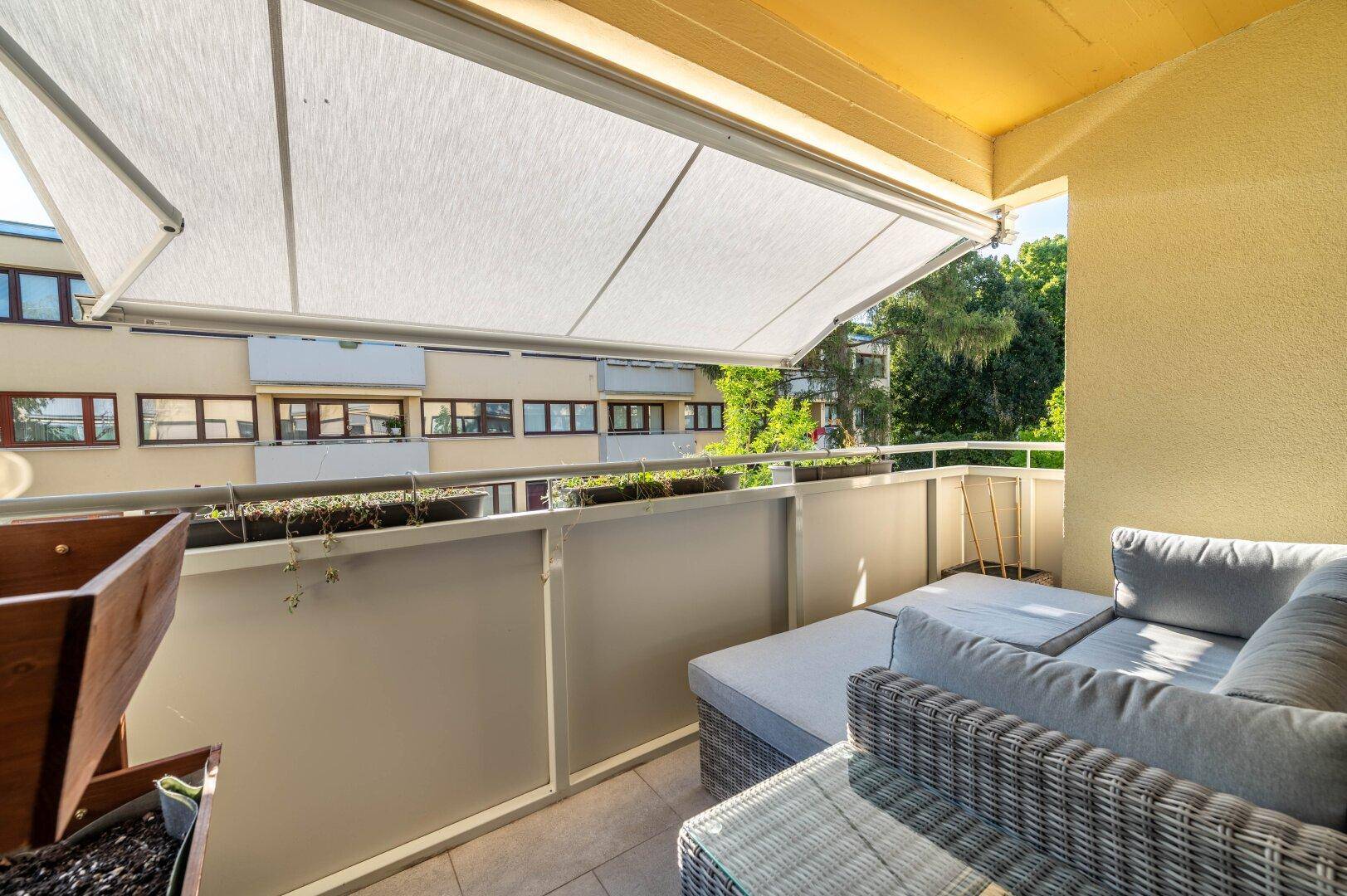 Sonniger Balkon mit bequemen Loungemöbeln und ausfahrbarer Markise.