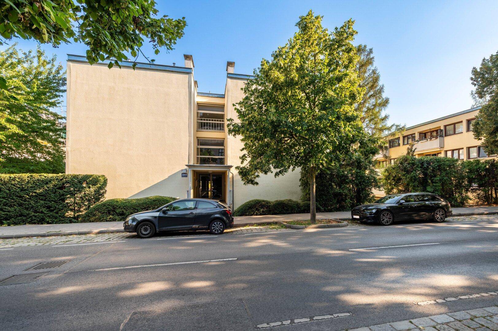 Wohngebäude mit gepflegter Fassade, Bäumen und parkenden Autos an der Straße.