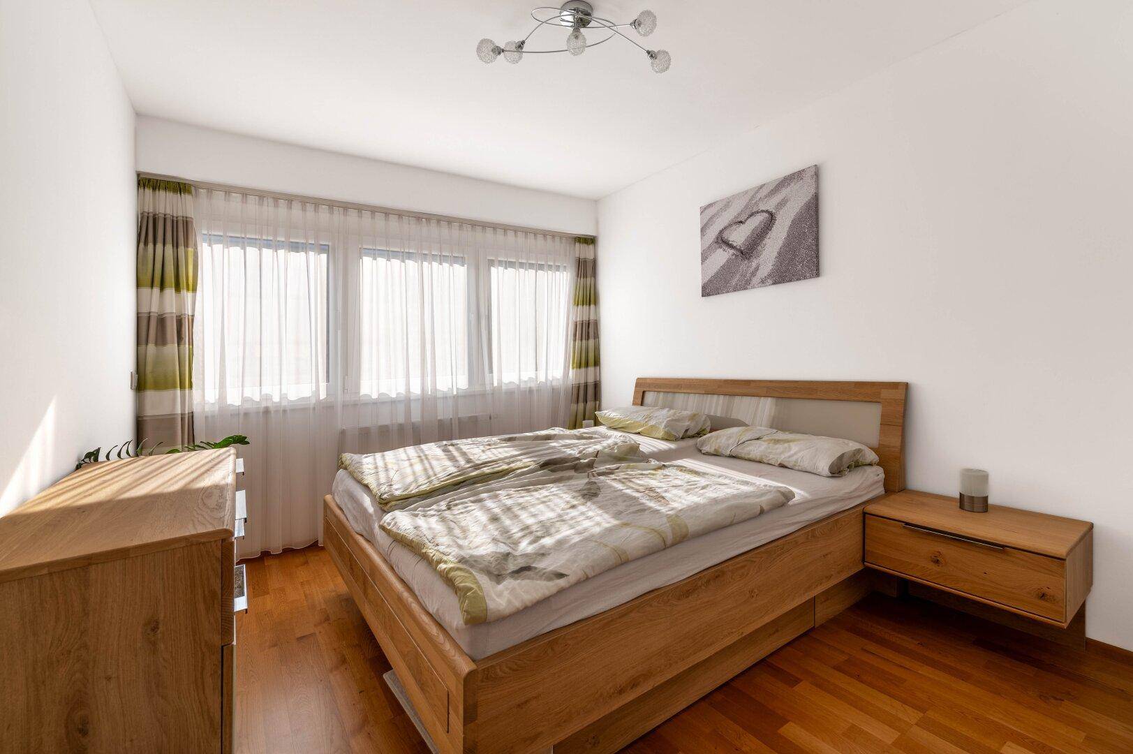 Helles Schlafzimmer mit Doppelbett, Holzmöbeln und großen Fenstern.