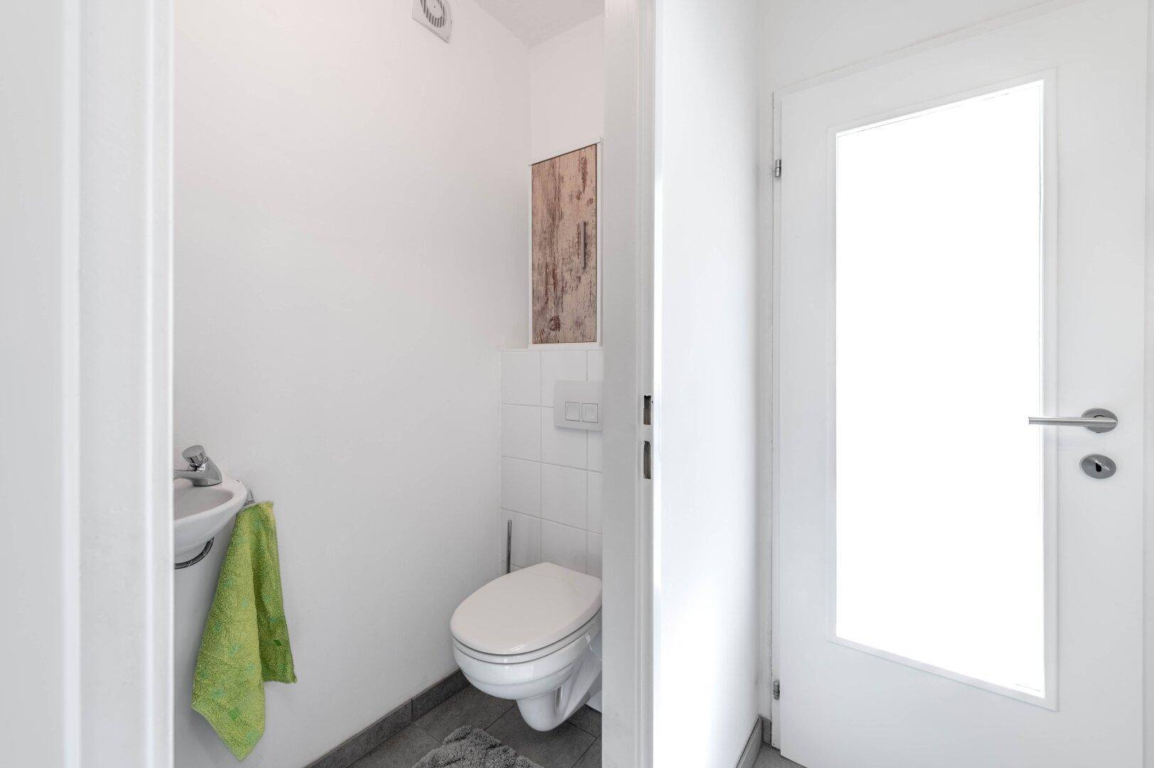 Kleines Gäste-WC mit Wand-WC, Waschbecken und Fliesenboden.