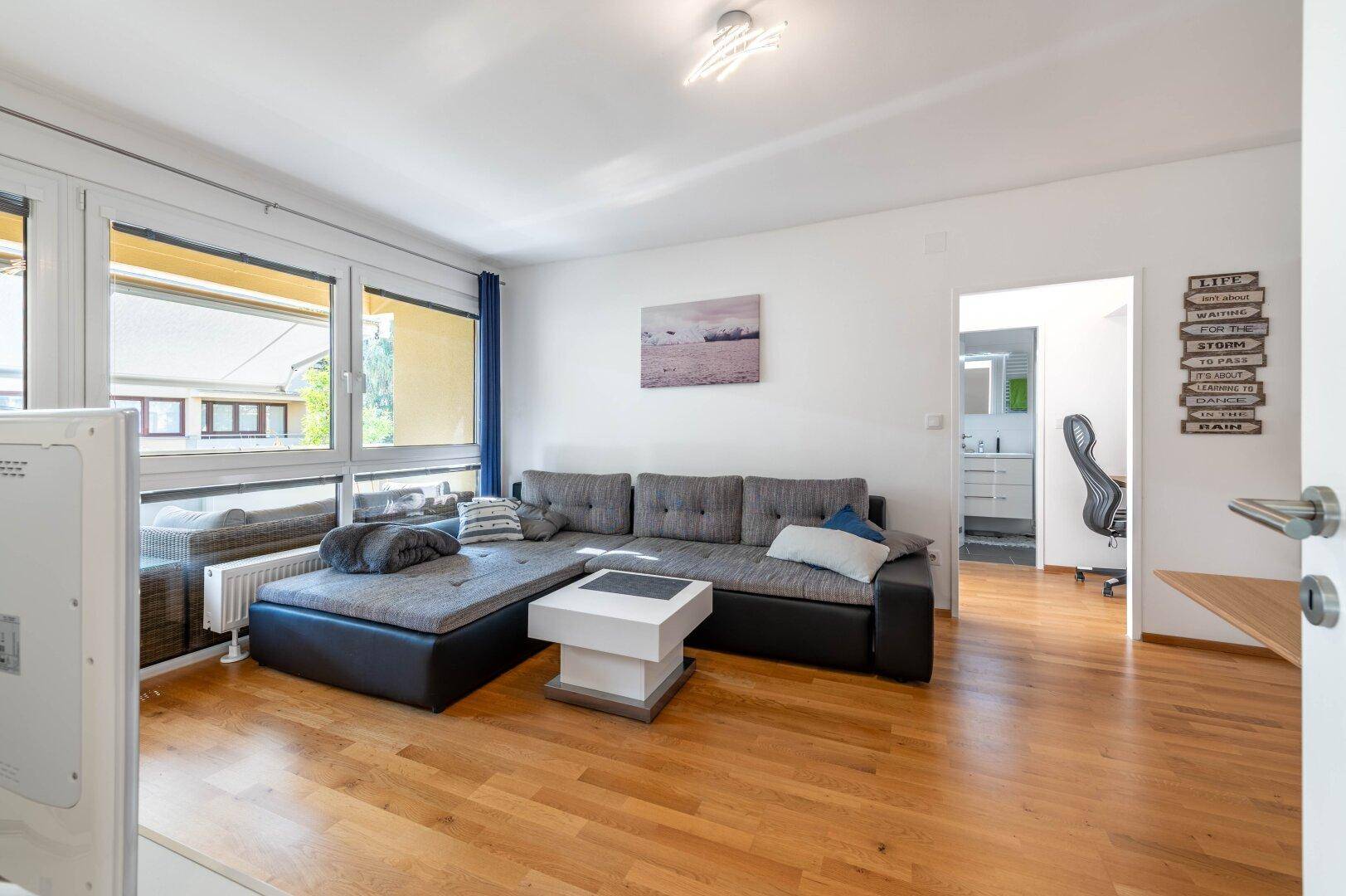Gemütliches Wohnzimmer mit großem Ecksofa, Holzboden und viel Tageslicht.