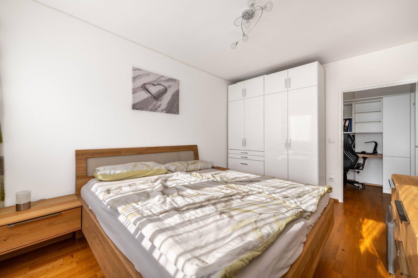 Schlafzimmer mit Holzbett, weißem Kleiderschrank und Zugang zum Arbeitszimmer.