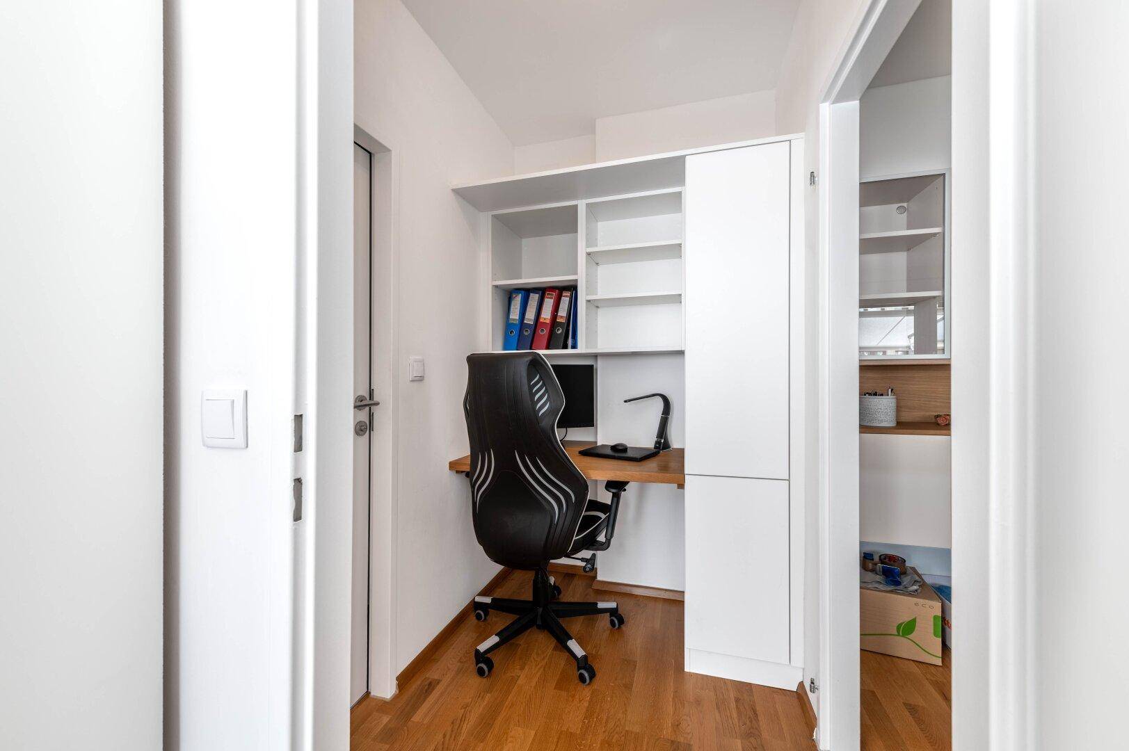 Kleines, helles Arbeitszimmer mit Schreibtisch, Regal und Holzboden.