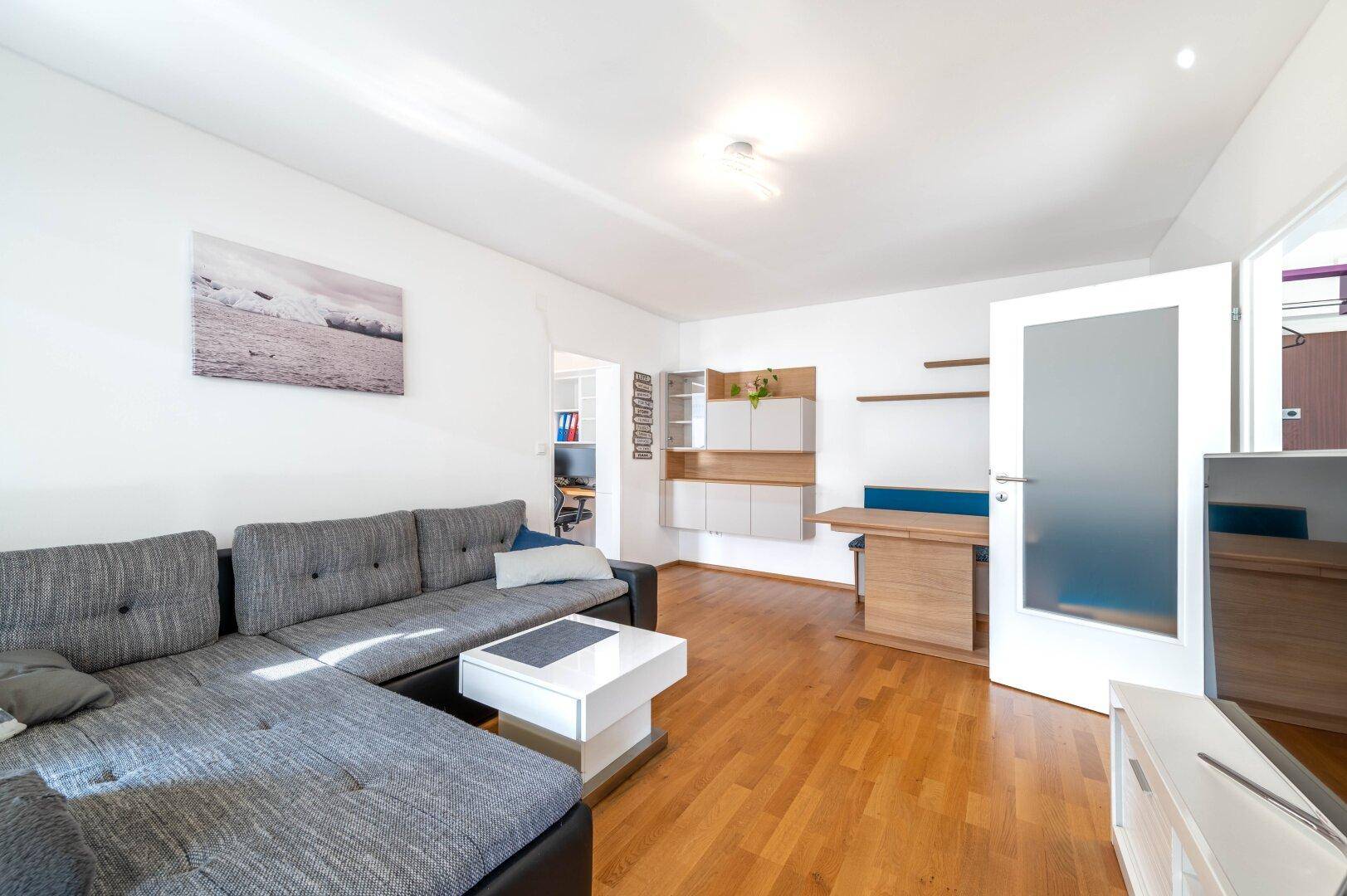 Geräumiger Wohnbereich mit Sofa, Esstisch und Zugang zu einem weiteren Zimmer.