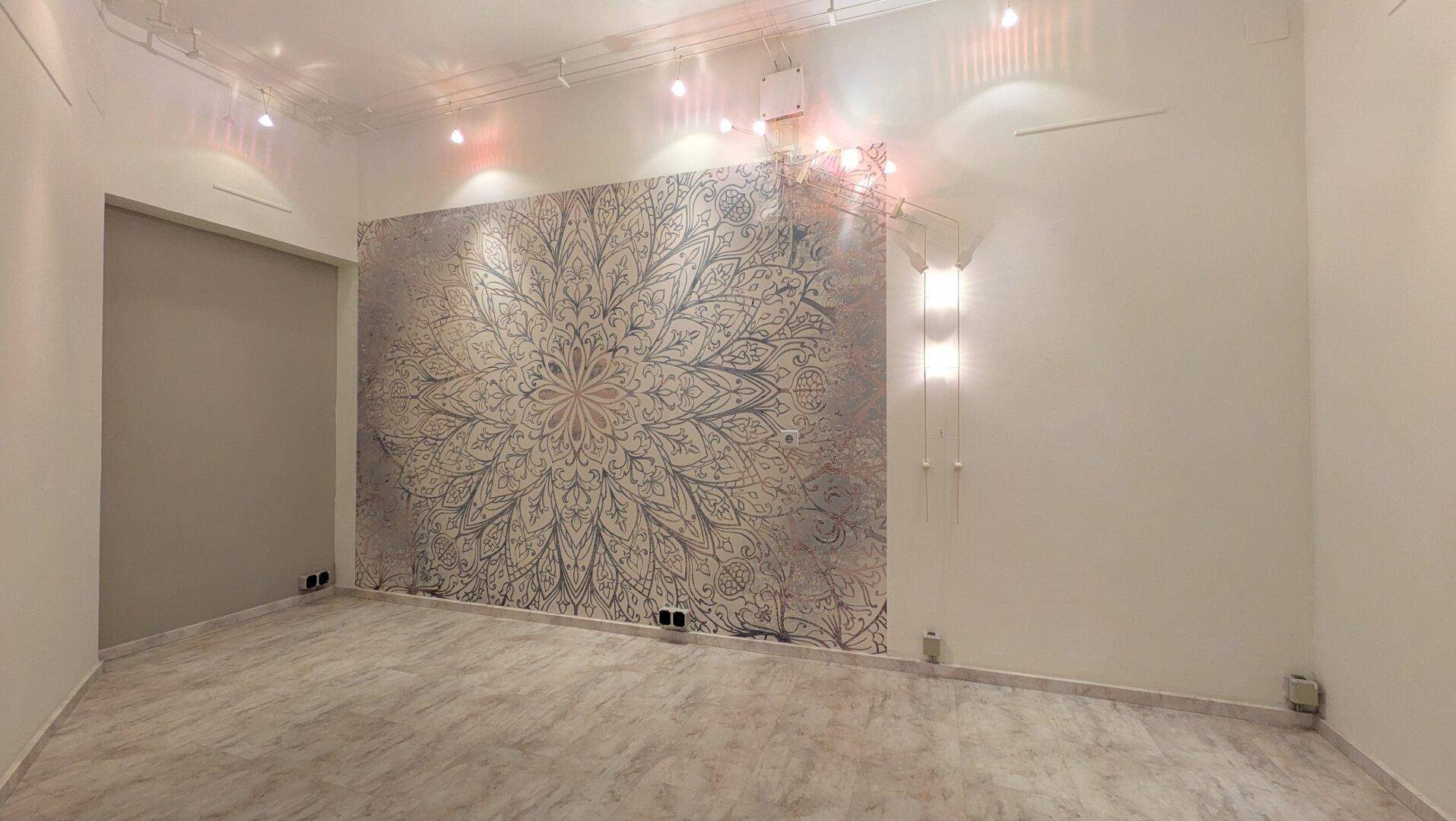 Leerer Raum mit großem Mandala-Wandbild, Fliesenboden und Schienenbeleuchtung, bereit zur Nutzung.