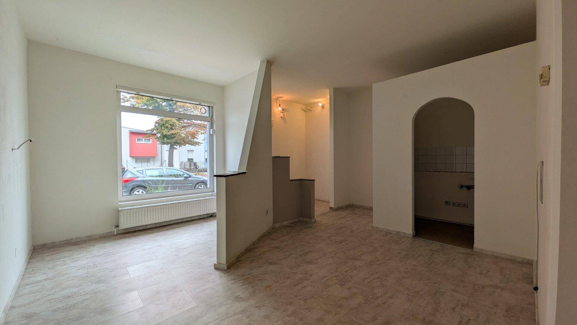 Leerer Geschäftsraum mit großen Fenstern, Fliesenboden und einem Durchgang mit Bogen.