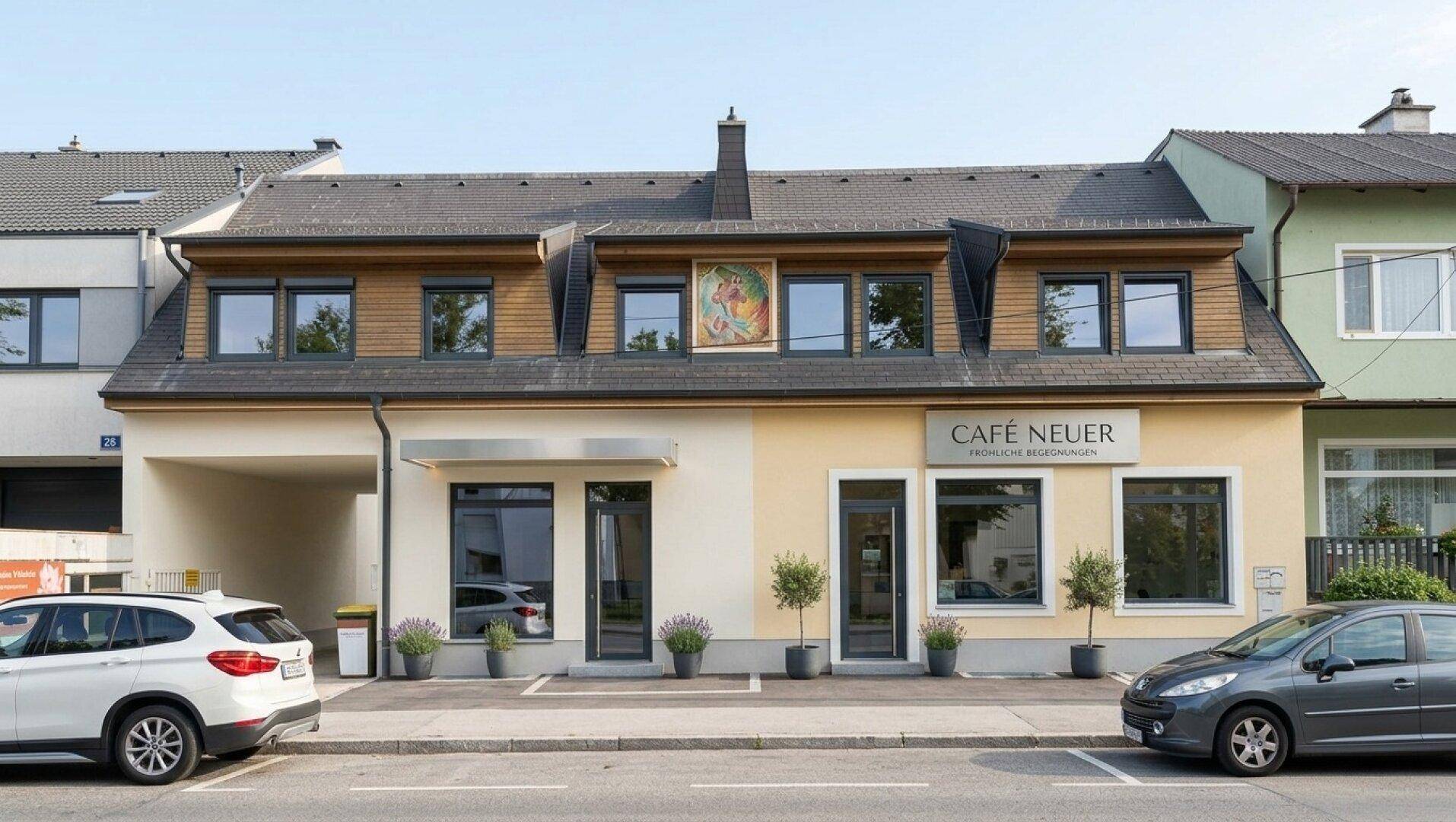 Ansicht eines Geschäftsgebäudes mit Café im Erdgeschoss und Wohnungen darüber, an einer belebten Straße gelegen.