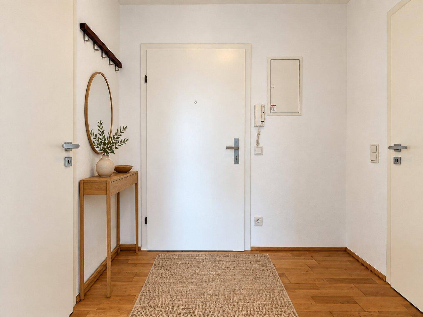 Eingangsbereich mit Holzboden, weißer Tür und Gegensprechanlage.