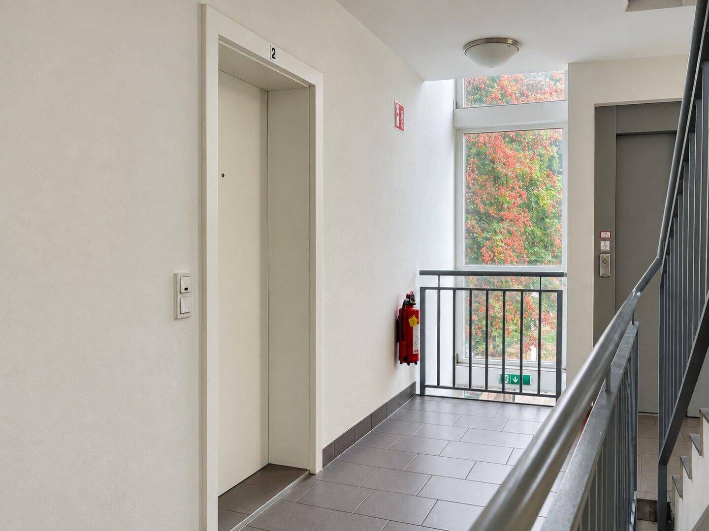 Heller Flur im Treppenhaus mit Aufzug und Blick ins Freie.