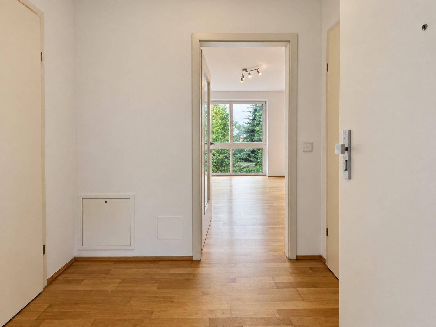 Leerer Eingangsbereich mit Holzboden und Blick in den hellen Wohnbereich.