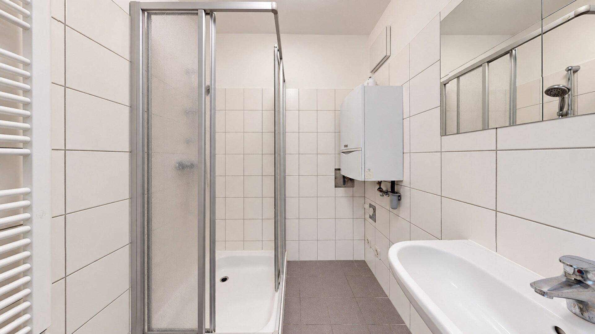 Leeres Badezimmer mit Duschkabine, Waschbecken und weißen Wandfliesen.