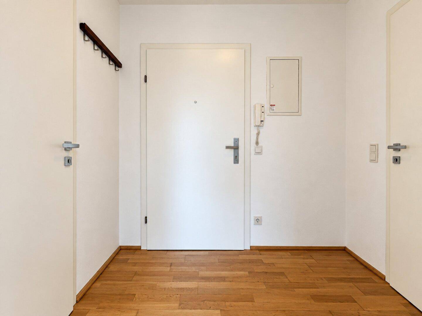 Leerer Eingangsbereich mit Holzboden und weißer Eingangstür.