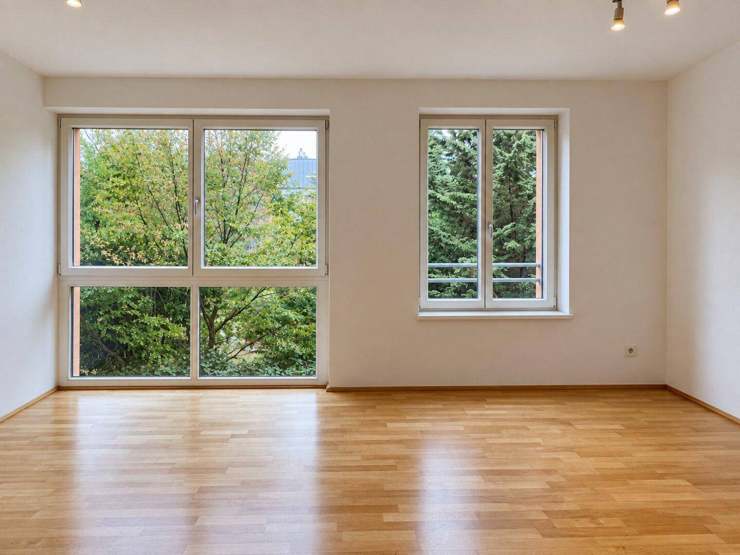 Geräumiges, leeres Wohnzimmer mit viel Tageslicht und Parkettboden.