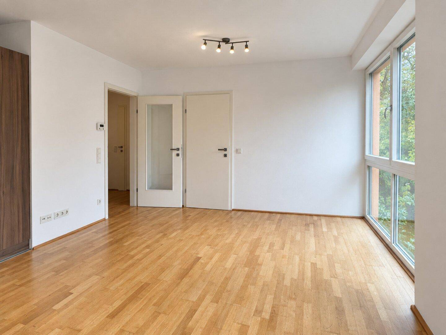 Leeres Wohnzimmer mit Holzboden und Zugang zu weiteren Räumen.