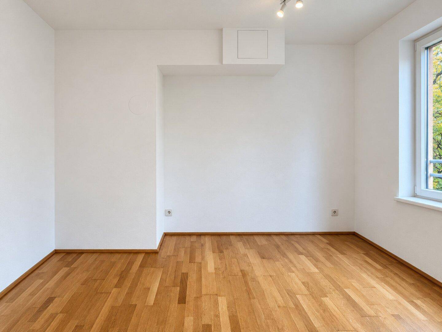 Leeres Schlafzimmer mit Holzboden und einem Fenster, das viel Licht spendet.