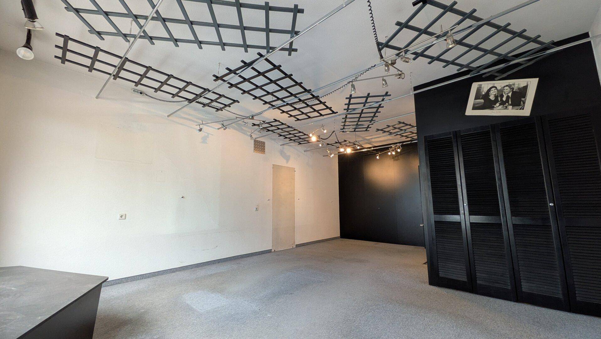 Leerer Ausstellungsraum mit Teppichboden, schwarzer Wand und dekorativen Lamellentüren, bereit für neue Präsentationen.