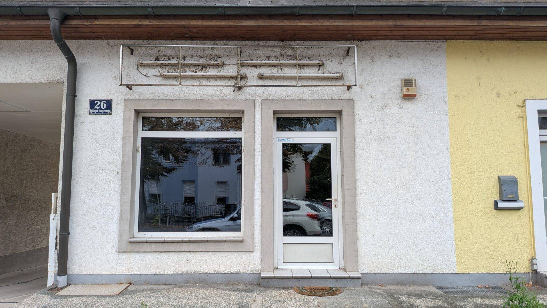 Fassade eines Geschäftsgebäudes mit großen Fenstern und einer Eingangstür, die auf eine frühere Nutzung hinweist.