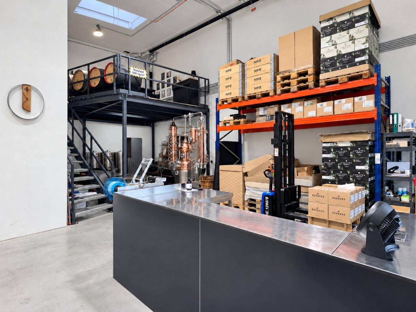 Industrieller Produktionsbereich mit Kupferbrennblase, Lagerregalen, einer Galerieebene und Holzfässern.