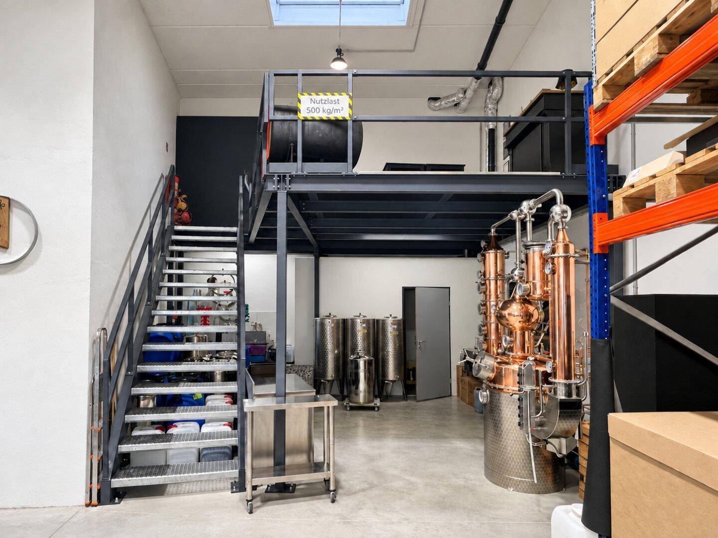 Produktionshalle mit großer Kupferbrennblase, Edelstahltanks und einer Metalltreppe zur oberen Galerie.