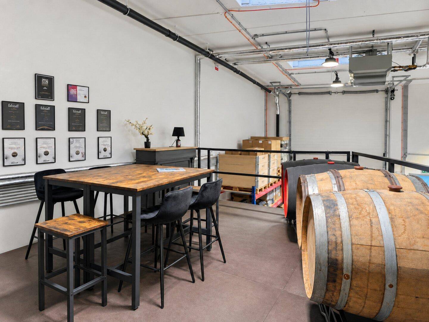 Detailansicht des Loungebereichs auf der Galerie mit modernem Stehtisch, Hockern und gerahmten Zertifikaten.