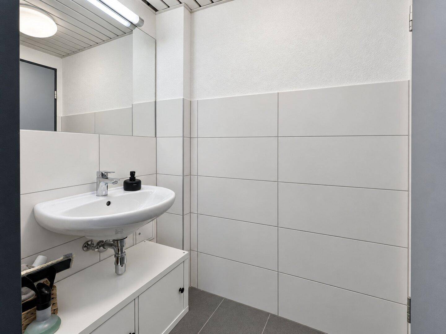 Modernes Badezimmer mit weißen Wandfliesen, grauem Boden und einem wandmontierten Waschbecken.