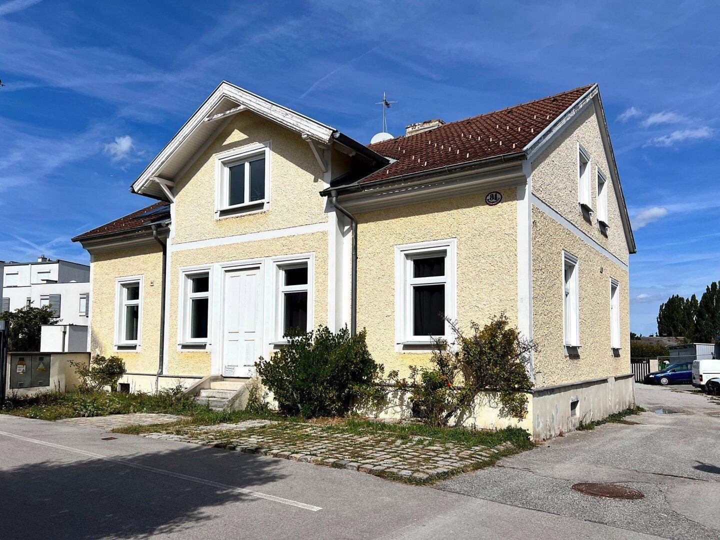 Seitenansicht des charmanten gelben Hauses mit Ziegeldach und gepflegter Fassade unter blauem Himmel.