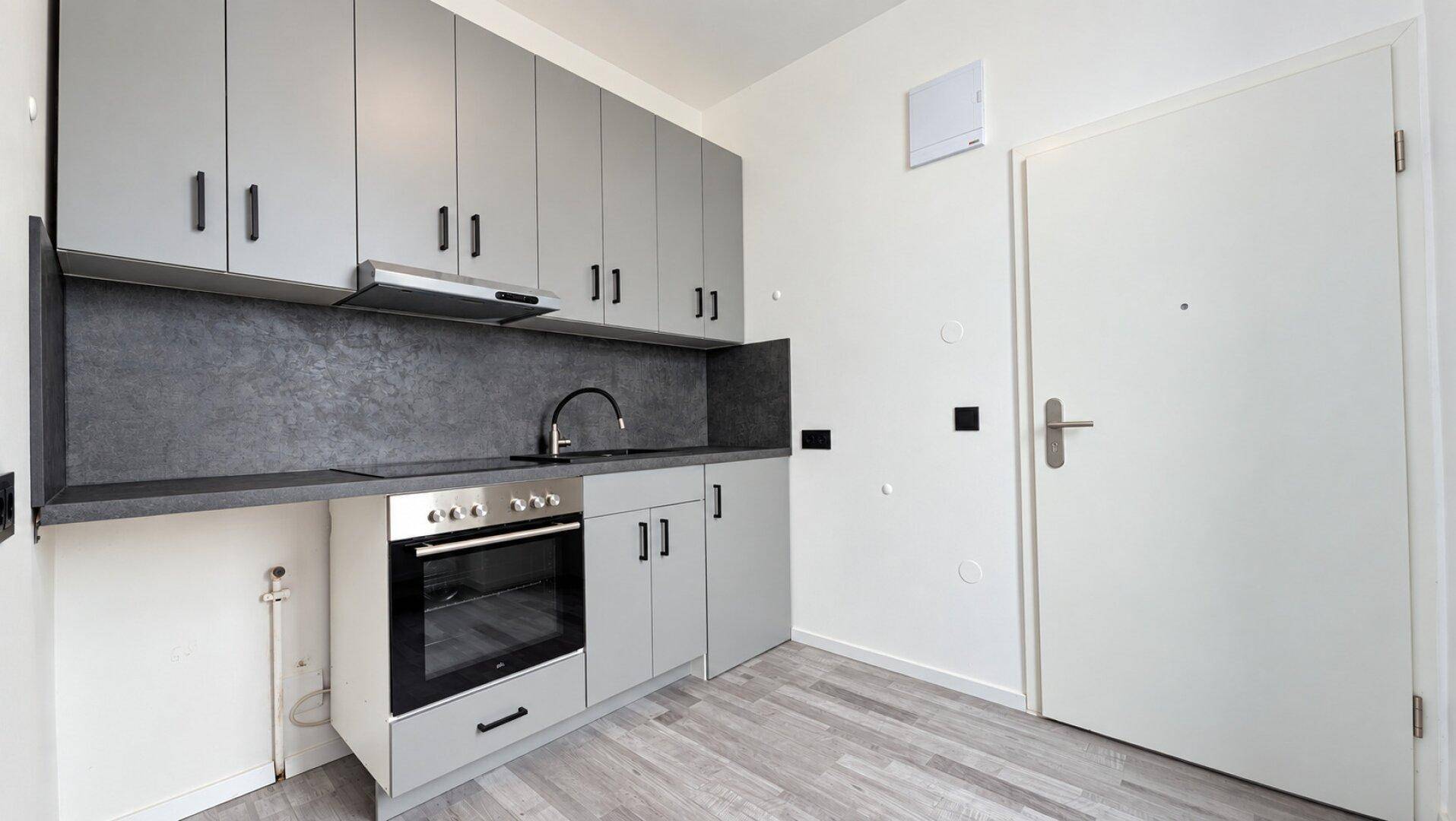 Funktionale, moderne Küche mit grauen Schränken, integriertem Backofen und Spüle.